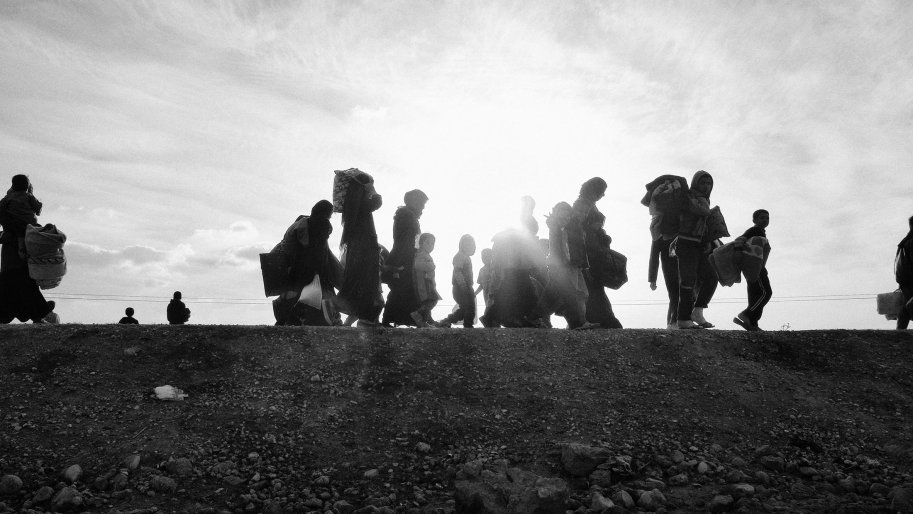 Photo en noir et blanc. Des personnes déplacées marchent en direction du camp d'Ain Issa.