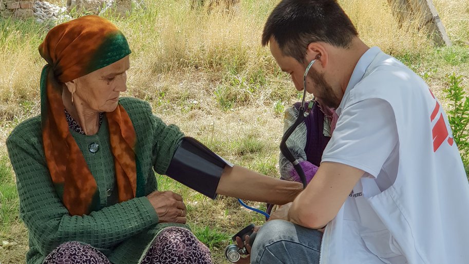 Un staff MSF prend la tension d’une dame âgée assise par terre