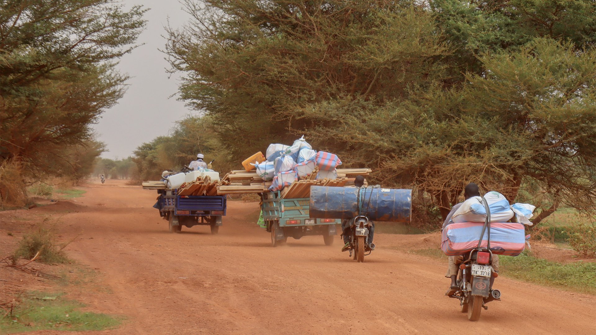Sur une route de terre, deux motos et deux tricycles chargés des kits distribués par MSF roulent en sens opposé.