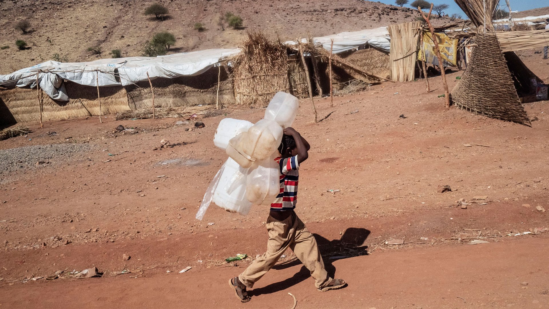 Ein Kind trägt Wasserkanister zur nächsten Wasserstelle im Flüchtlingslager Um Rakuba.