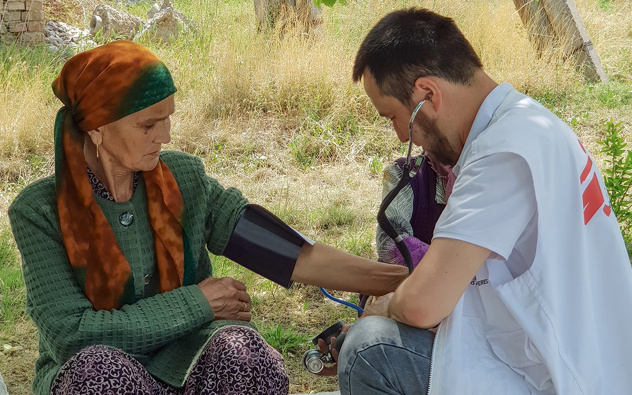 Un staff MSF prend la tension d’une dame âgée assise par terre