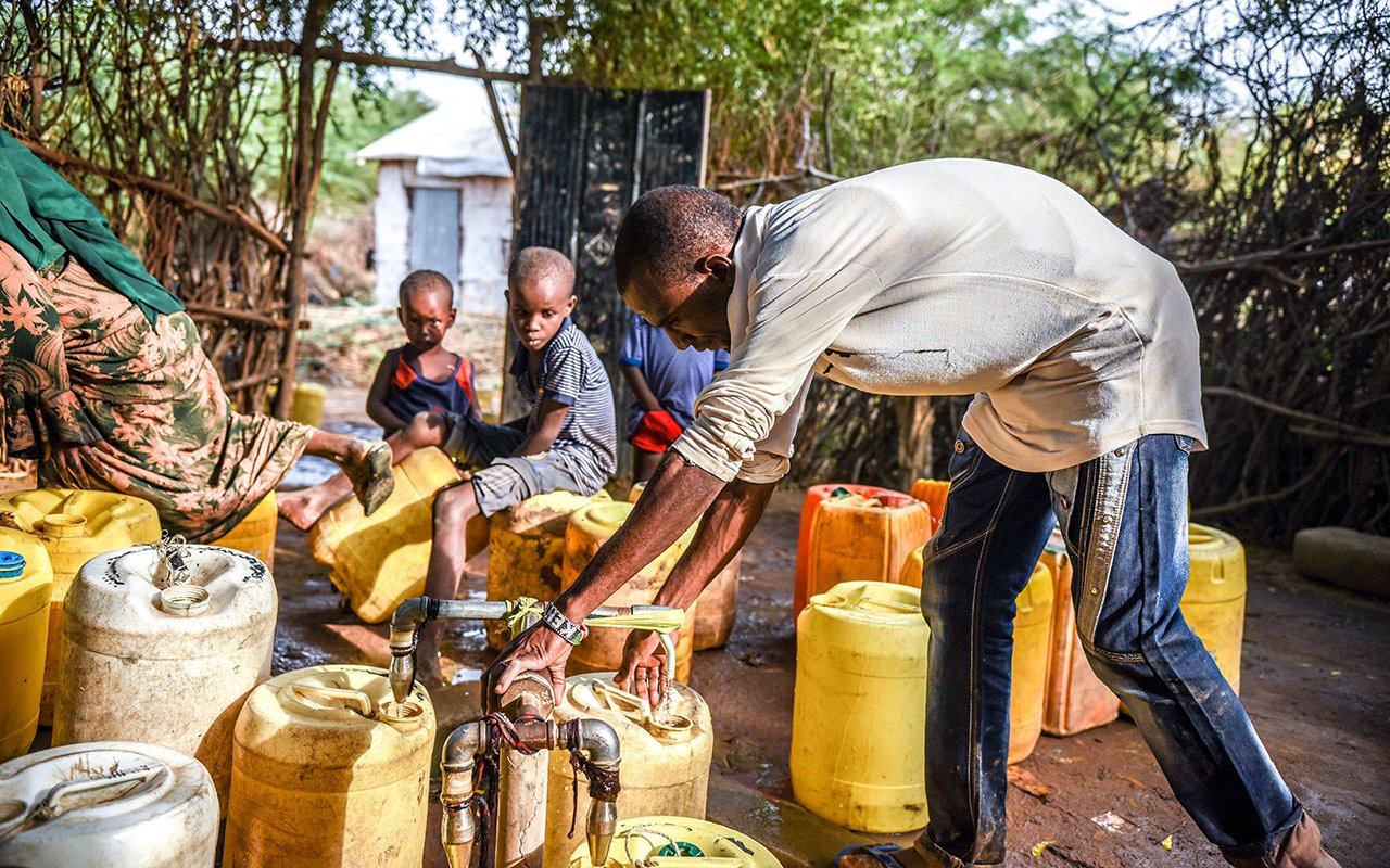 Un homme rempli des bidons d’eau sous le regard d’enfants en arrière-plan