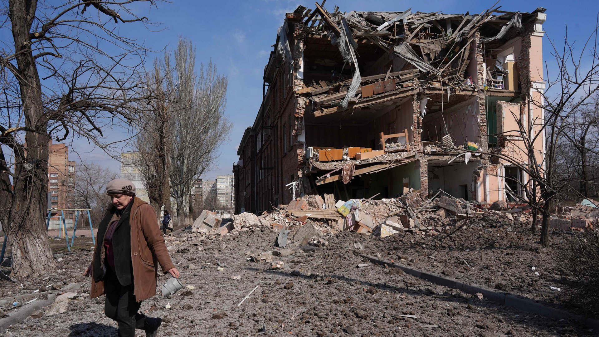 Une femme marche devant un immeuble ravagée par les bombes.