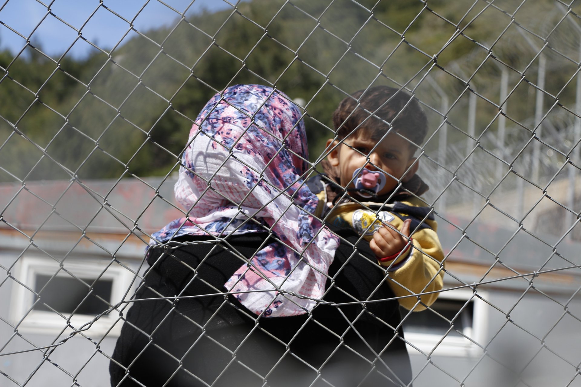 Eine syrische Mutter und ihr Kind hinter dem Drahtzaun rund um das Camp auf der griechischen Insel Samos, in dem Geflüchtete und Asylsuchende leben. Das Foto entstand im März 2016.