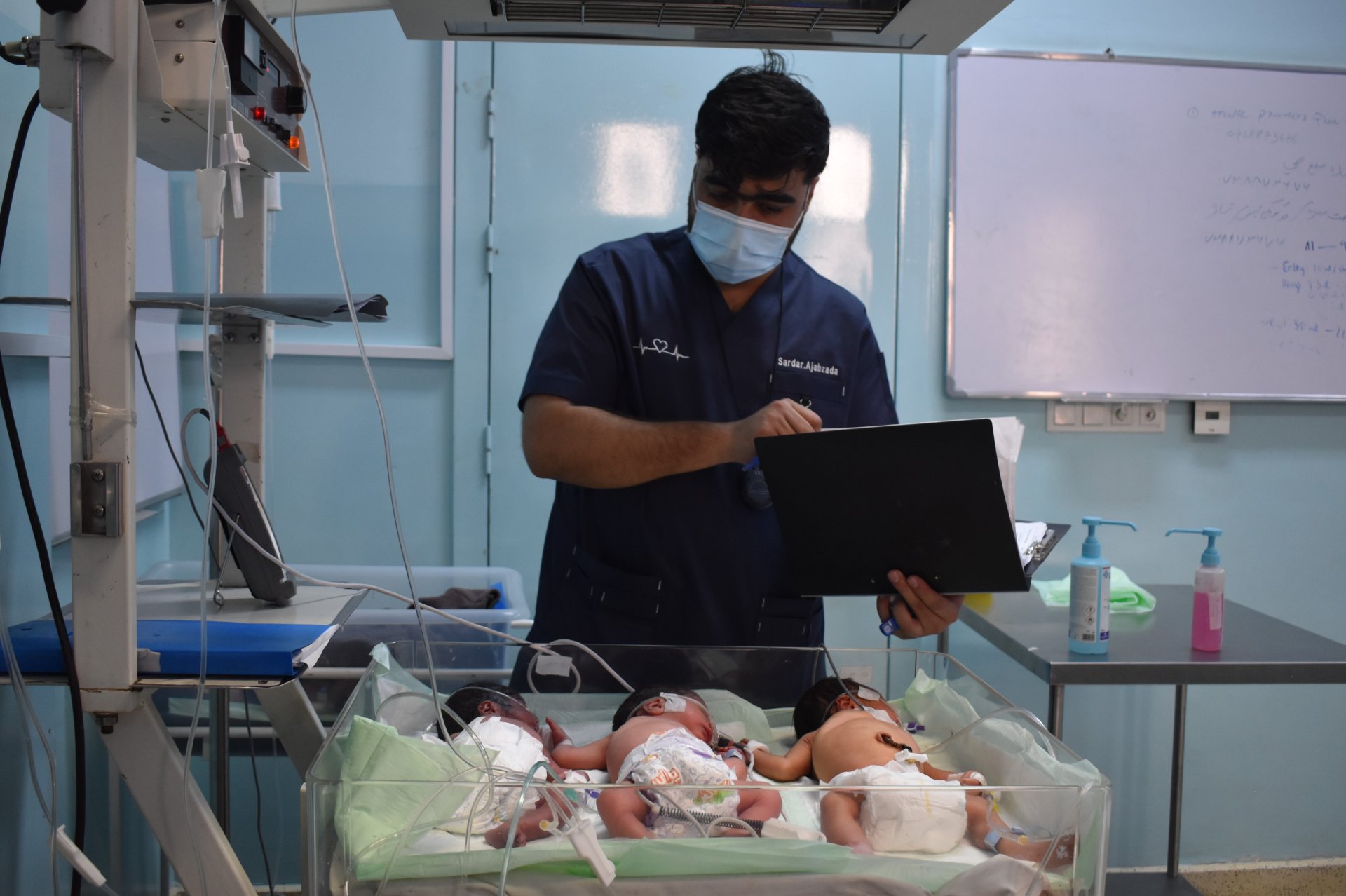 Un médecin observe trois bébés partageant le même lit chauffant dans un hôpital.