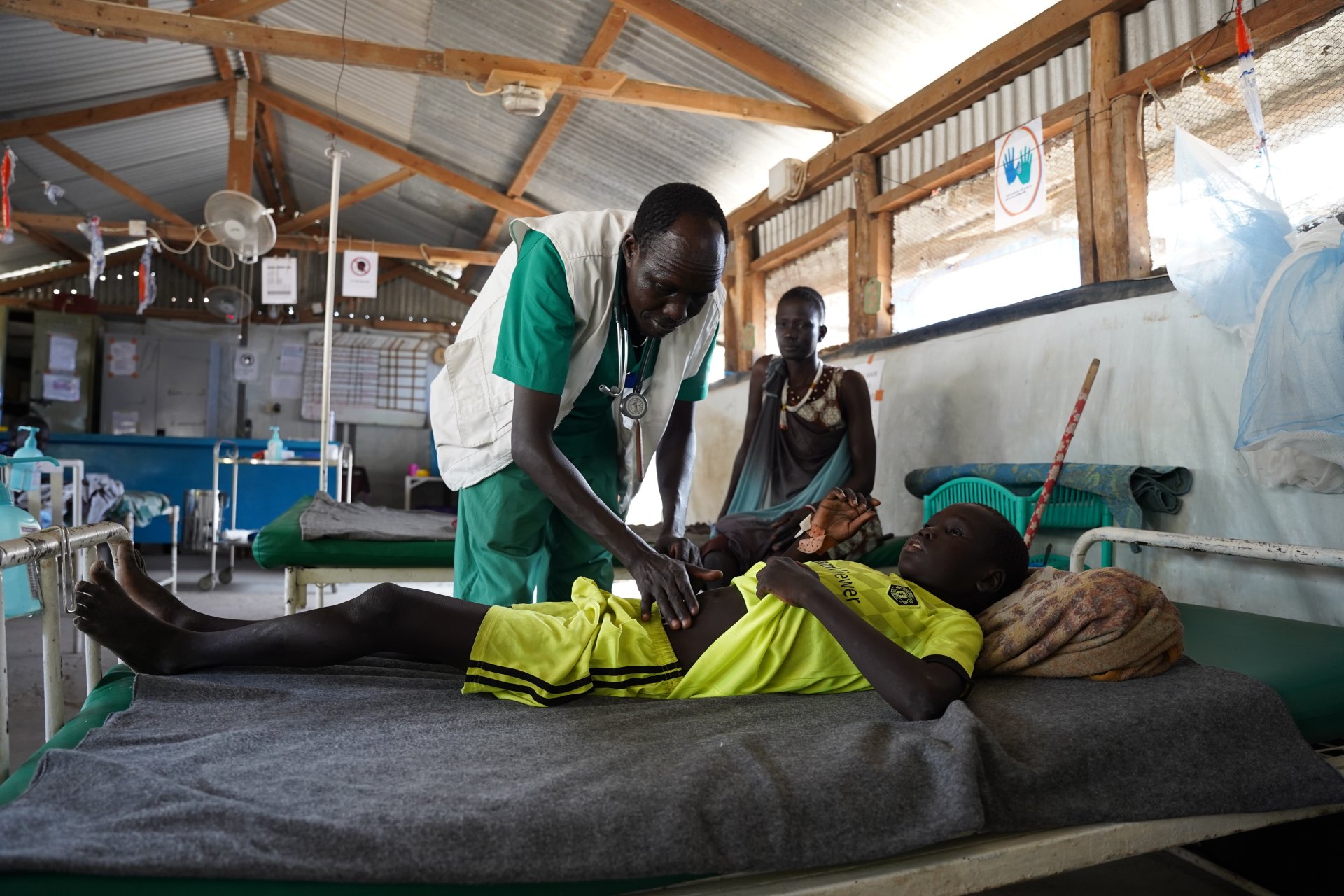Bang Bol, superviseur de l'équipe infirmière de MSF, examine Nhial Mayiel, 11 ans, sous le regard de sa mère. Le garçon est soigné à l'hôpital MSF de Lankien, situé dans l'État de Jonglei, au Soudan du Sud.