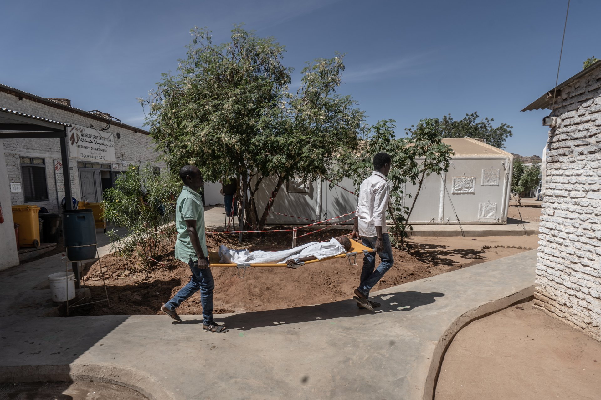 Deux membres du personnel médical de MSF transportent un jeune garçon sur une civière depuis le bloc opératoire vers l'unité de soins intensifs de l'hôpital de Paris géré par MSF à Tawila