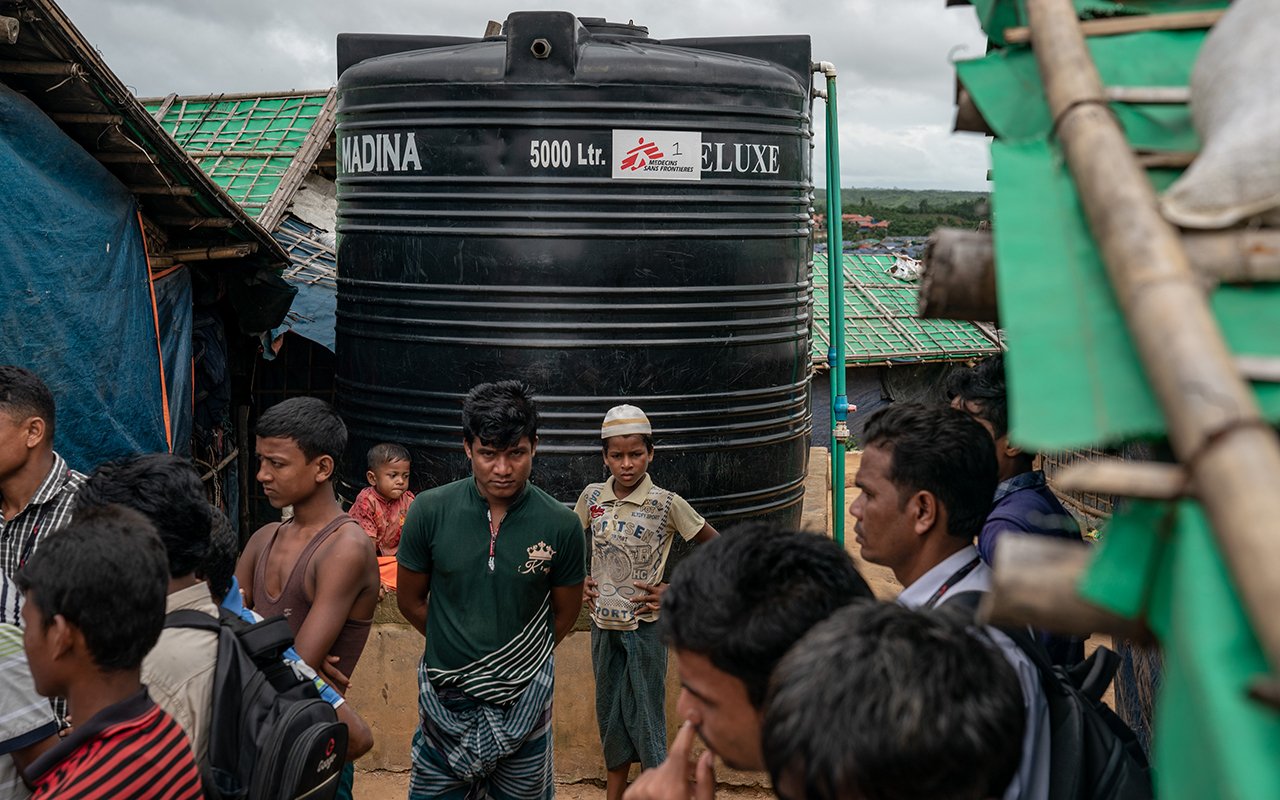 Un homme regarde fixement l’objectif, devant une grande citerne d’eau en arrière-plan.