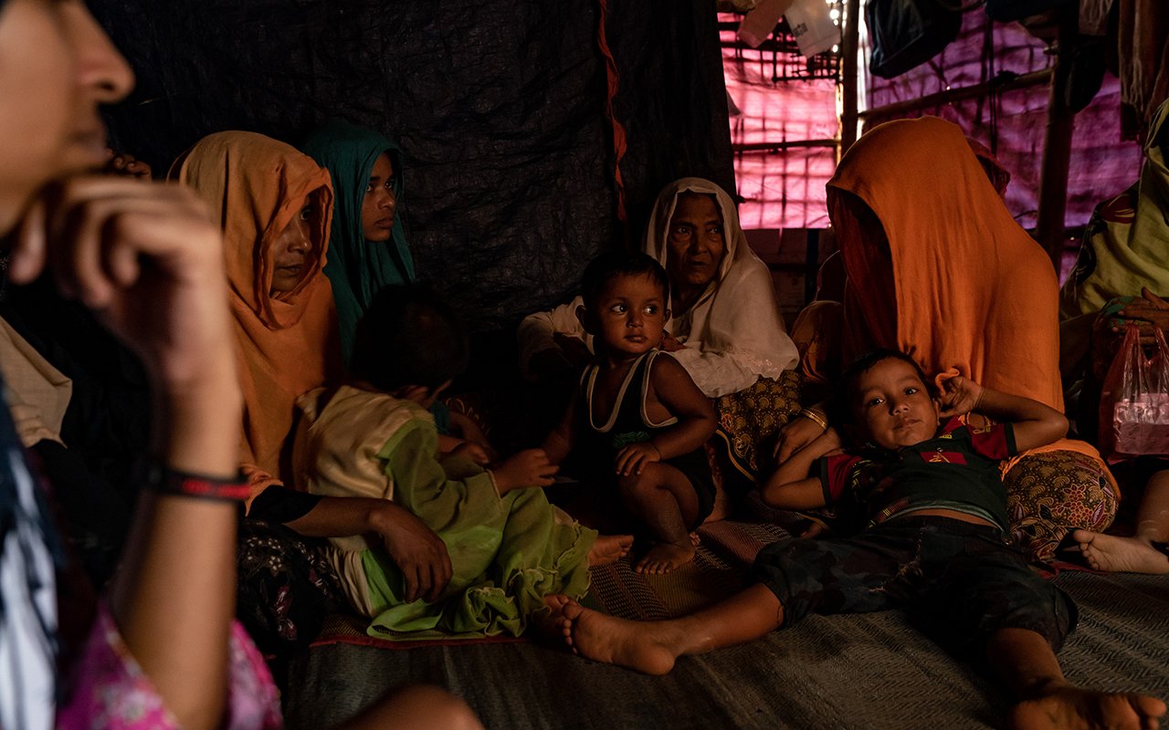 Des femmes et des enfants assis par terre écoutent un interlocuteur hors-champ