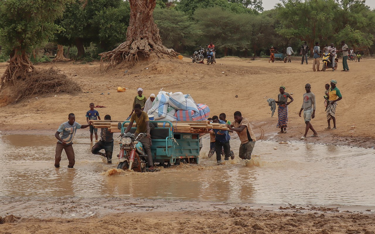 Des hommes poussent un tricycle motorisé à travers une rivière