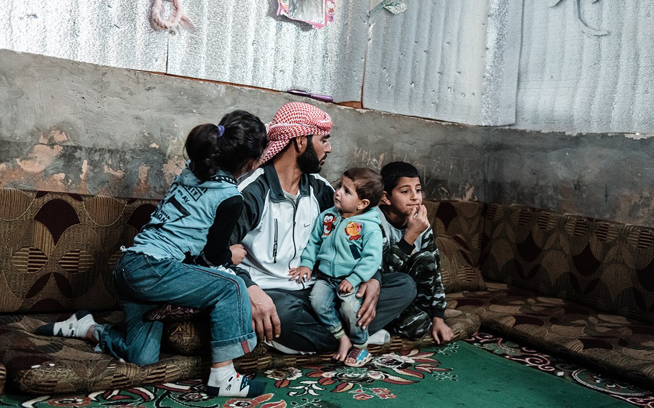 Ein Mann sitz mit seinen drei Kindern in ihrer provisorischen Unterkunft.