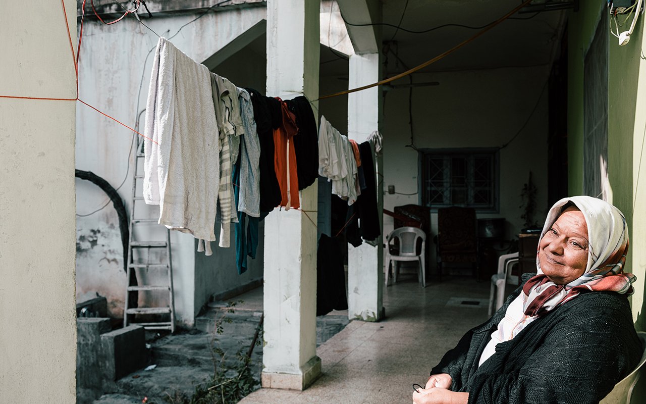 Une femme assise sur une chaise en plastique, avec du linge accroché à une corde en arrière-plan