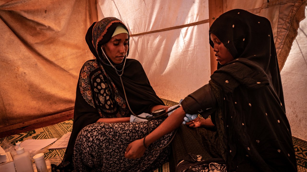 In einem Zelt wird eine junge Frau von einer MSF Mitarbeiterin auf ihren Puls untersucht.