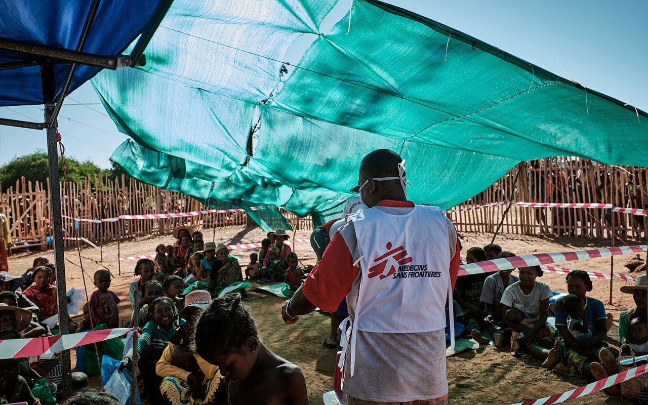 Des patients attendent leurs consultations assis sous des bâches, sous l’œil vigilant d’un staff MSF qui organise l’ordre de passage. 