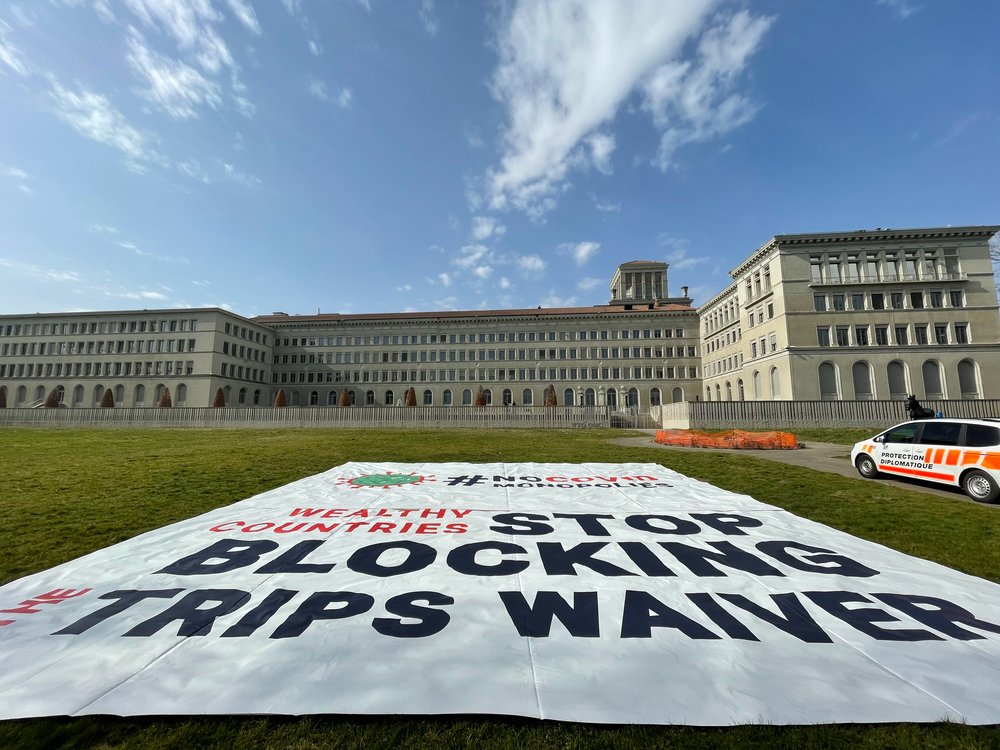 Stop Blocking Trips Waiver Poster in front of the WTO building in Geneva
