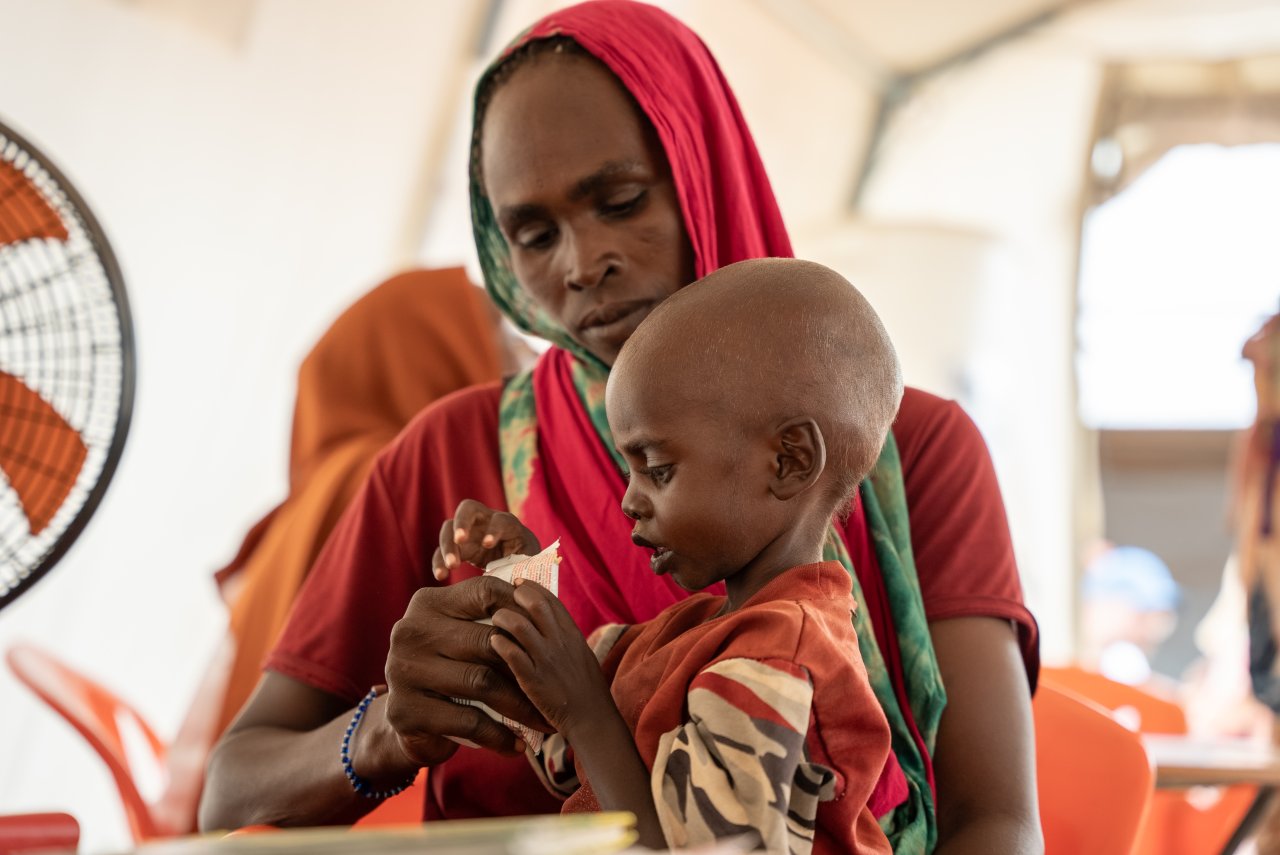 Mère avec son enfant mangeant du plumpy-nut, une pâte à base d'arachide dans un emballage plastique pour le traitement de la malnutrition aiguë sévère, dans la clinique MSF du camp d'Adre.