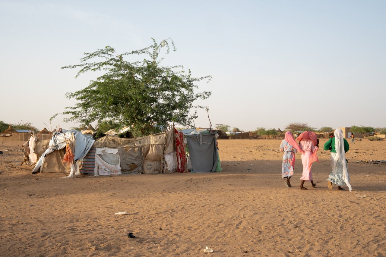 Dans le camp de réfugiés, des femmes passent devant des abris de fortune construits à partir de carton, de toiles de jute, de tissu et de bâches en plastique. 