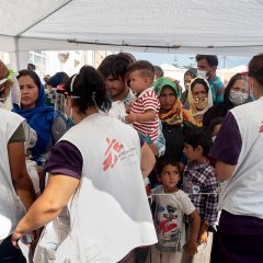 3 staffs MSF accueillent des patients qui font la queue sous une tente.