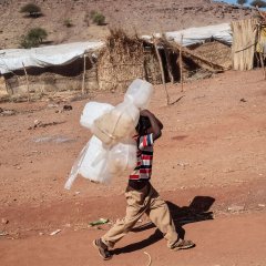 Un enfant marche avec des jerrycans en plastique sur le dos dans le camp de réfugiés de Um Rakuba.