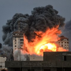 Des personnes se trouvant sur un toit regardent une boule de feu et de fumée s'élever au-dessus d'un immeuble dans la ville de Gaza le 7 octobre 2023 lors d'une frappe aérienne israélienne qui a touché l'immeuble Palestine Tower.