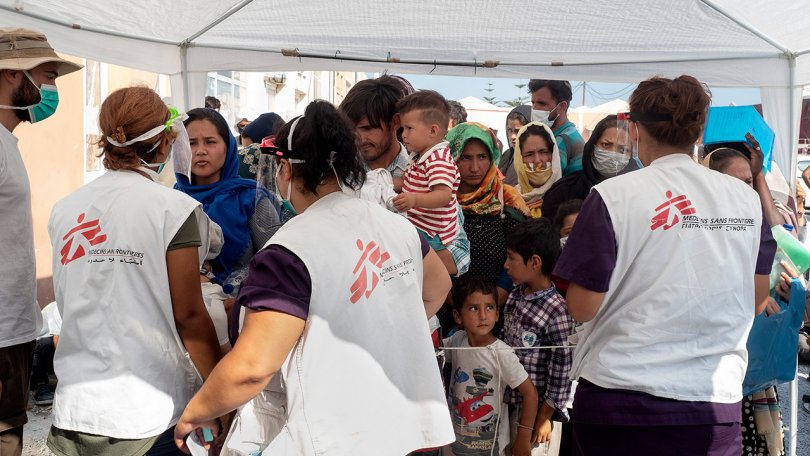 3 staffs MSF accueillent des patients qui font la queue sous une tente.