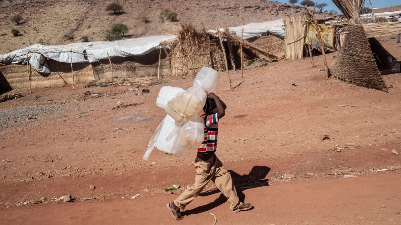 Ein Kind trägt Wasserkanister zur nächsten Wasserstelle im Flüchtlingslager Um Rakuba.
