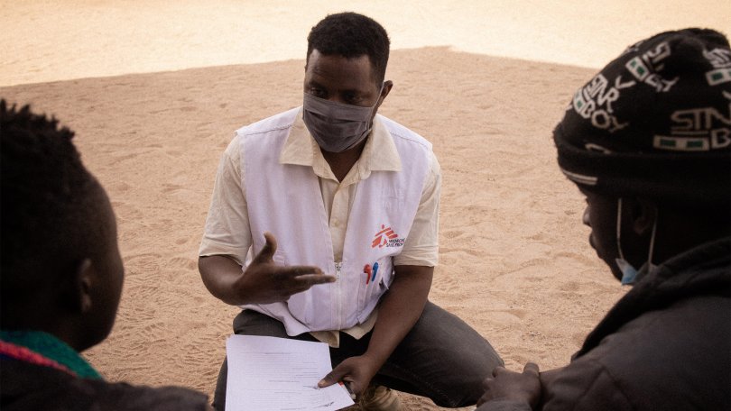 Issuf erklärt zwei Migrant:innen die Aktivitäten von MSF.