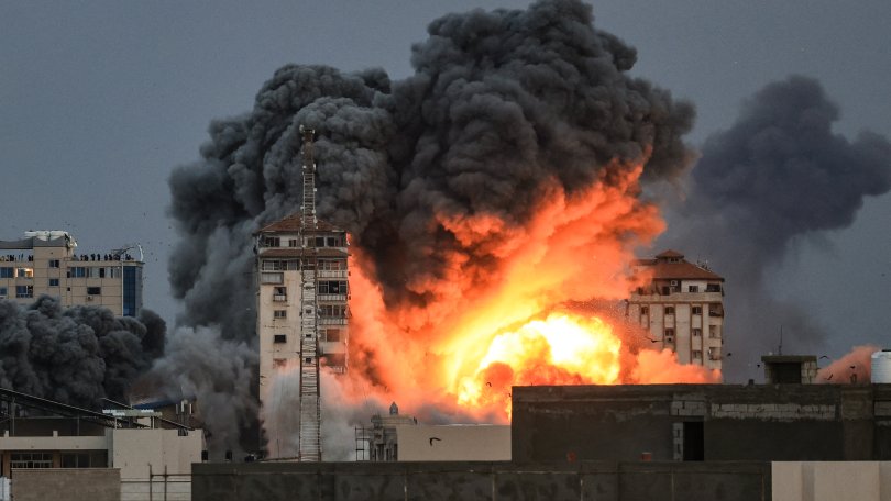 Des personnes se trouvant sur un toit regardent une boule de feu et de fumée s'élever au-dessus d'un immeuble dans la ville de Gaza le 7 octobre 2023 lors d'une frappe aérienne israélienne qui a touché l'immeuble Palestine Tower.