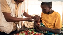 Un médecin de MSF examine Imani, âgée de 9 mois, qui a été admise à l'unité de nutrition thérapeutique intensive pour malnutrition aiguë sévère au poste de santé de MSF situé dans le camp de déplacés de Plaine Savo. Imani est assise sur les genoux de sa mère, Nehema, âgée de 20 ans, qui la tient dans ses bras pendant l'examen. 